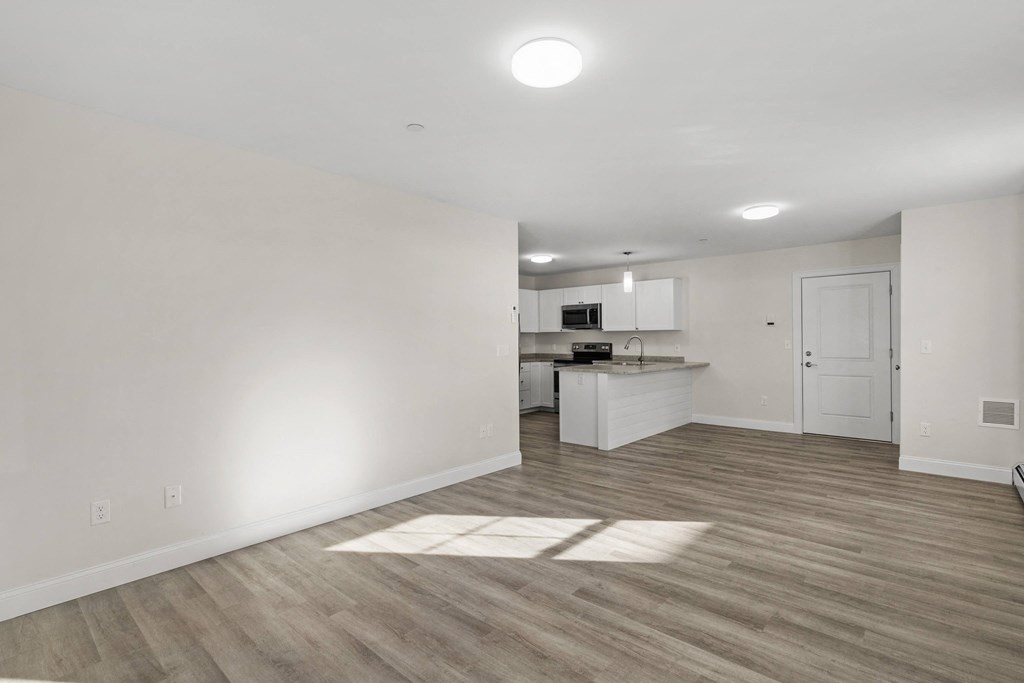 a living room and kitchen with white walls and wood flooring