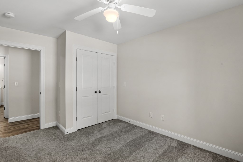 an empty living room with a ceiling fan and a door to a closet