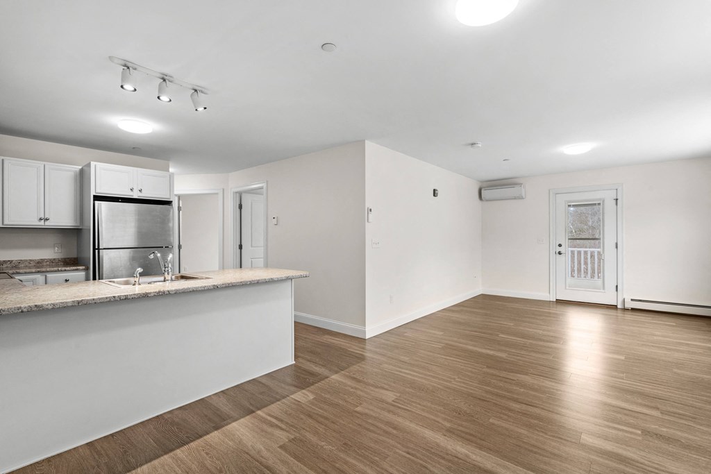 an empty living room and kitchen with a counter top and a refrigerator
