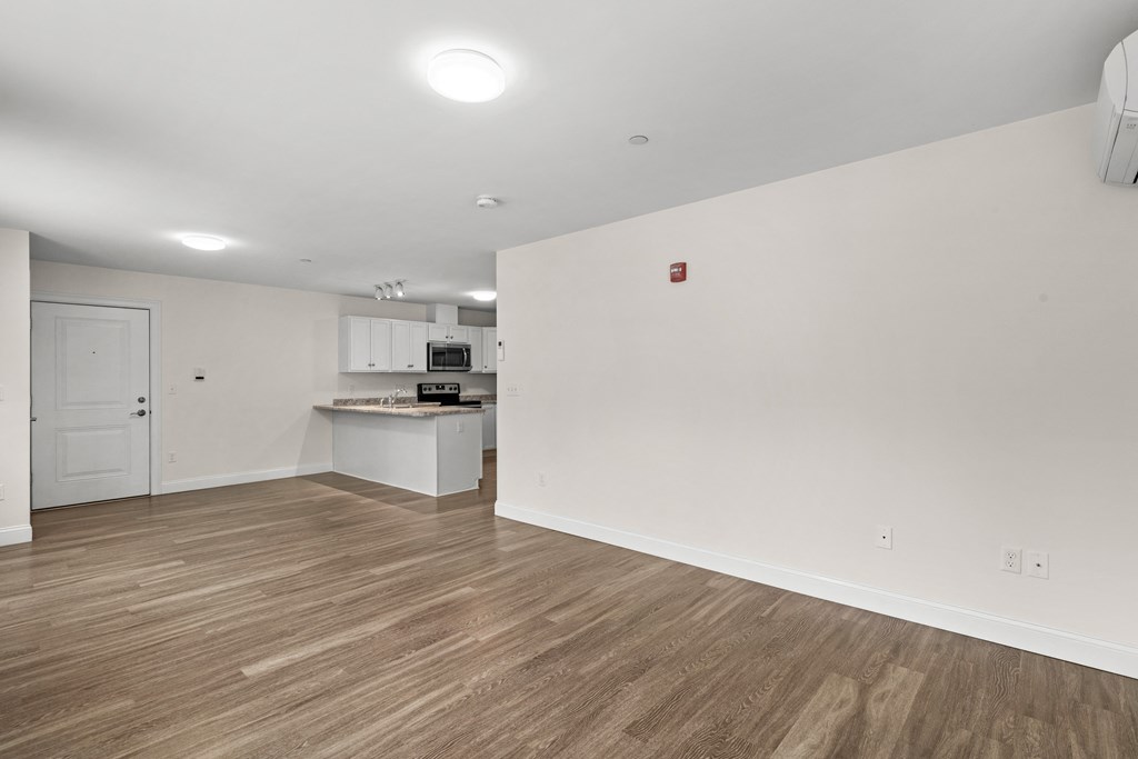 an empty living room and kitchen with white walls and wood flooring
