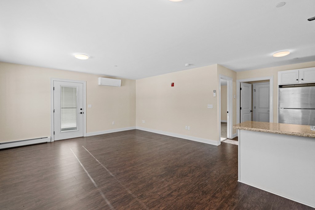 an empty living room with a kitchen and a refrigerator
