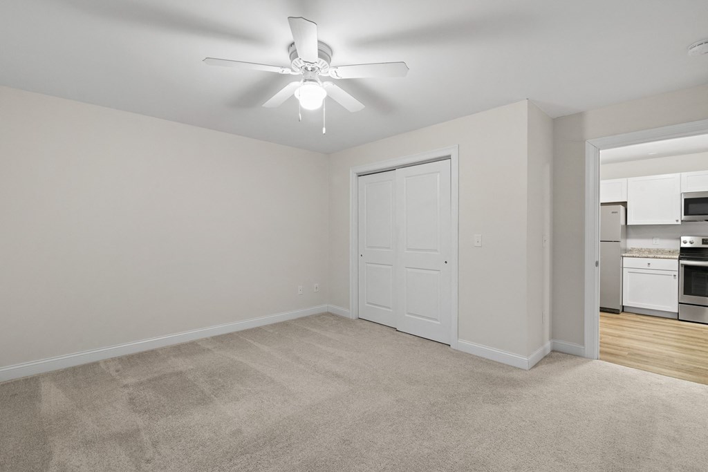 an empty living room with a ceiling fan and a kitchen