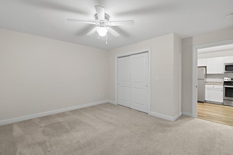 an empty living room with a ceiling fan and a kitchen