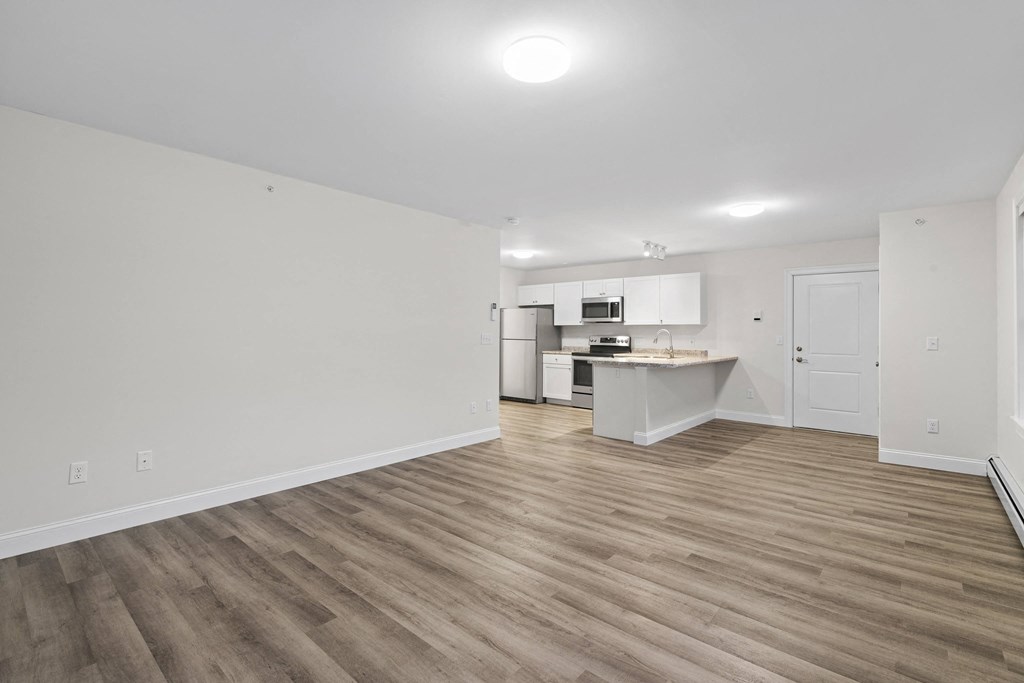 an empty living room and kitchen with white walls and wood flooring