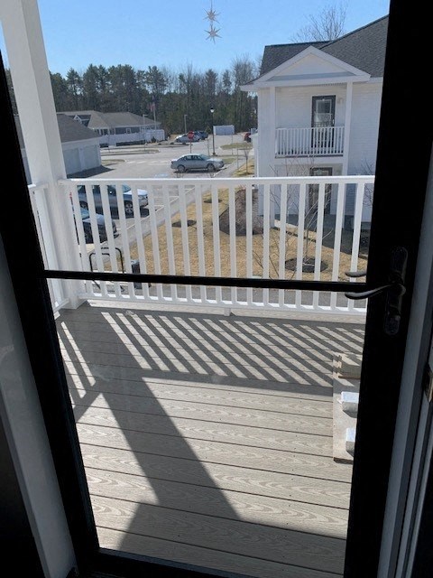 A view from a balcony looking out at a white house and cars in a parking lot.