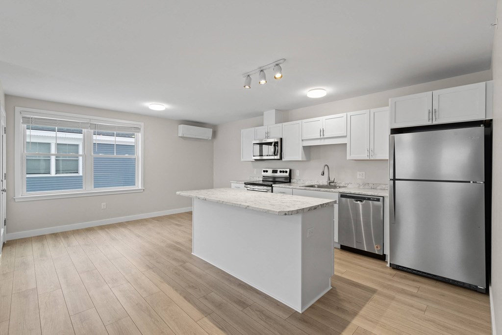a white kitchen with a large island and stainless steel refrigerator