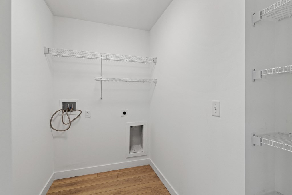 an empty room with white walls and wood flooring and a white closet with shelves