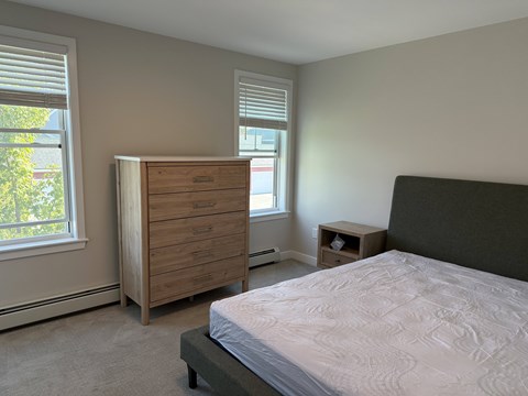 A bedroom with a bed, nightstand, and a wooden dresser.