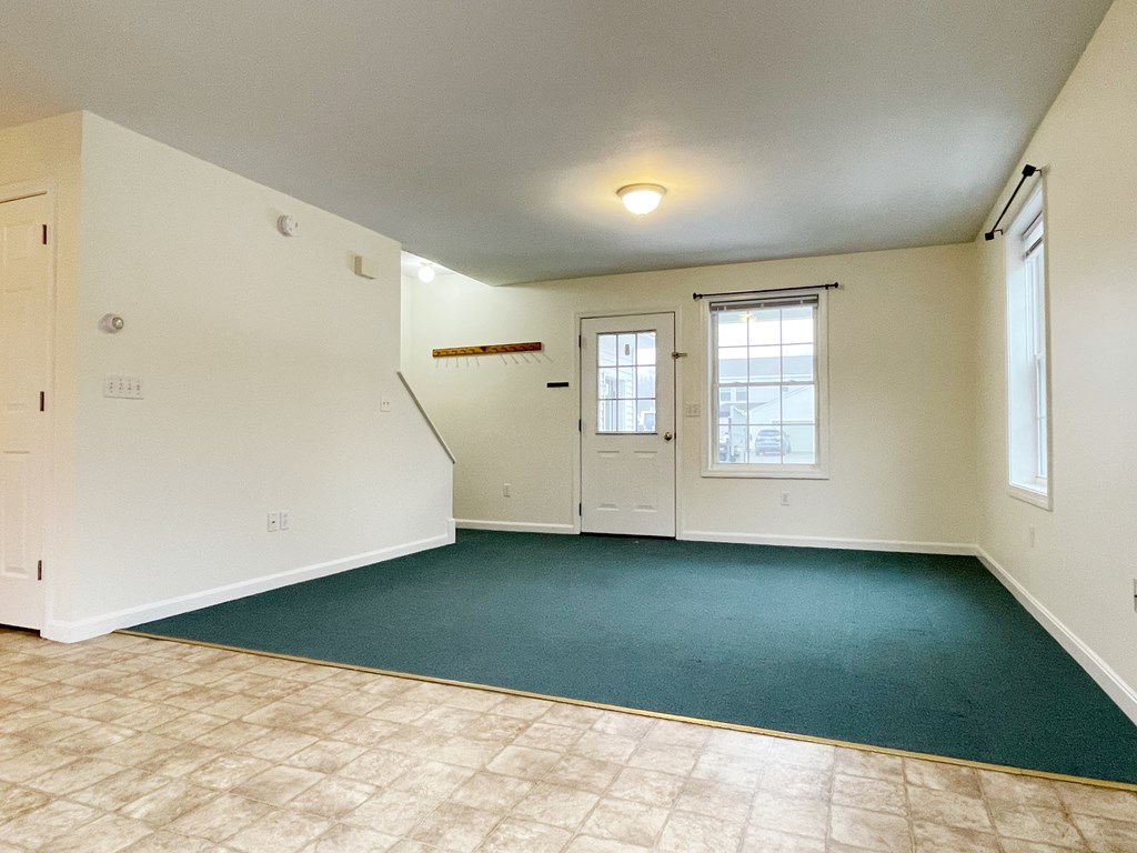 A room with a green carpet and a window with blinds.