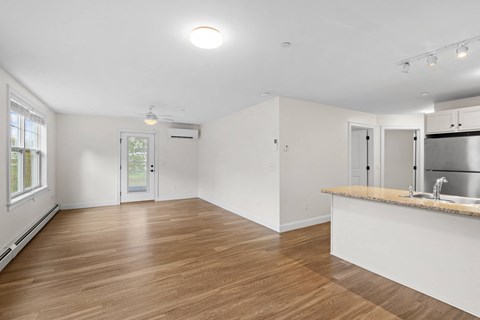 an empty living room and kitchen with a counter top and a refrigerator