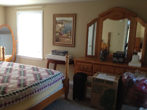 A bedroom with a bed, dresser, mirror, and a painting on the wall.