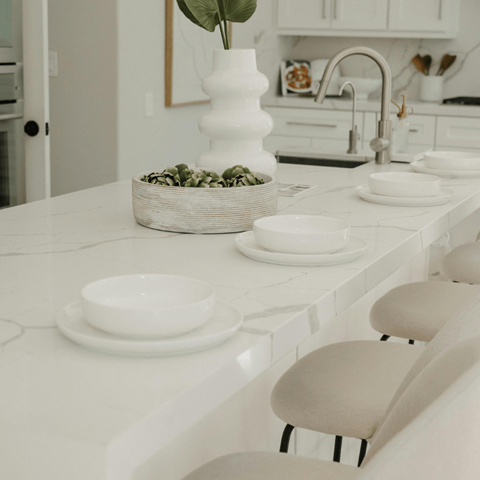 A white kitchen with a basket of green leaves on the counter.