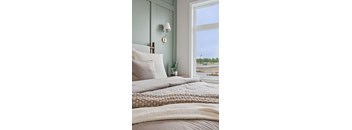 A bedroom with a bed, pillows, a lamp, and a window overlooking a parking lot.