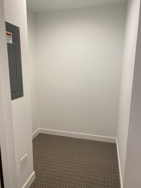 A white hallway with a door on the left and a strip of carpet on the floor.