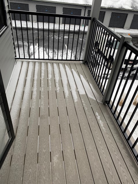 A wooden deck with a black railing and a view of a snowy street.