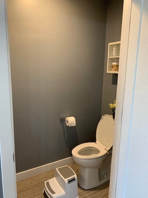 A white toilet with a grey trash can and toilet paper holder in a bathroom.