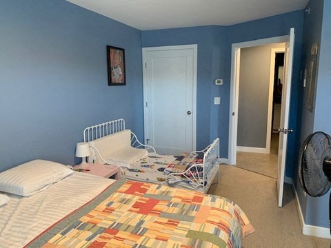 A bedroom with a bed, a fan, and a door.