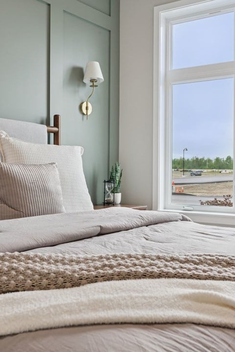 A bedroom with a bed, pillows, a lamp, and a window overlooking a parking lot.