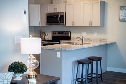 A kitchen with a countertop, bar stools, and a microwave above the stove.
