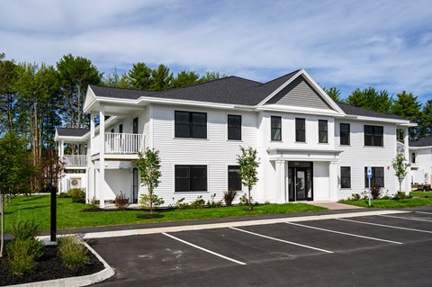 A white two-story building with a black roof and a parking lot in front.