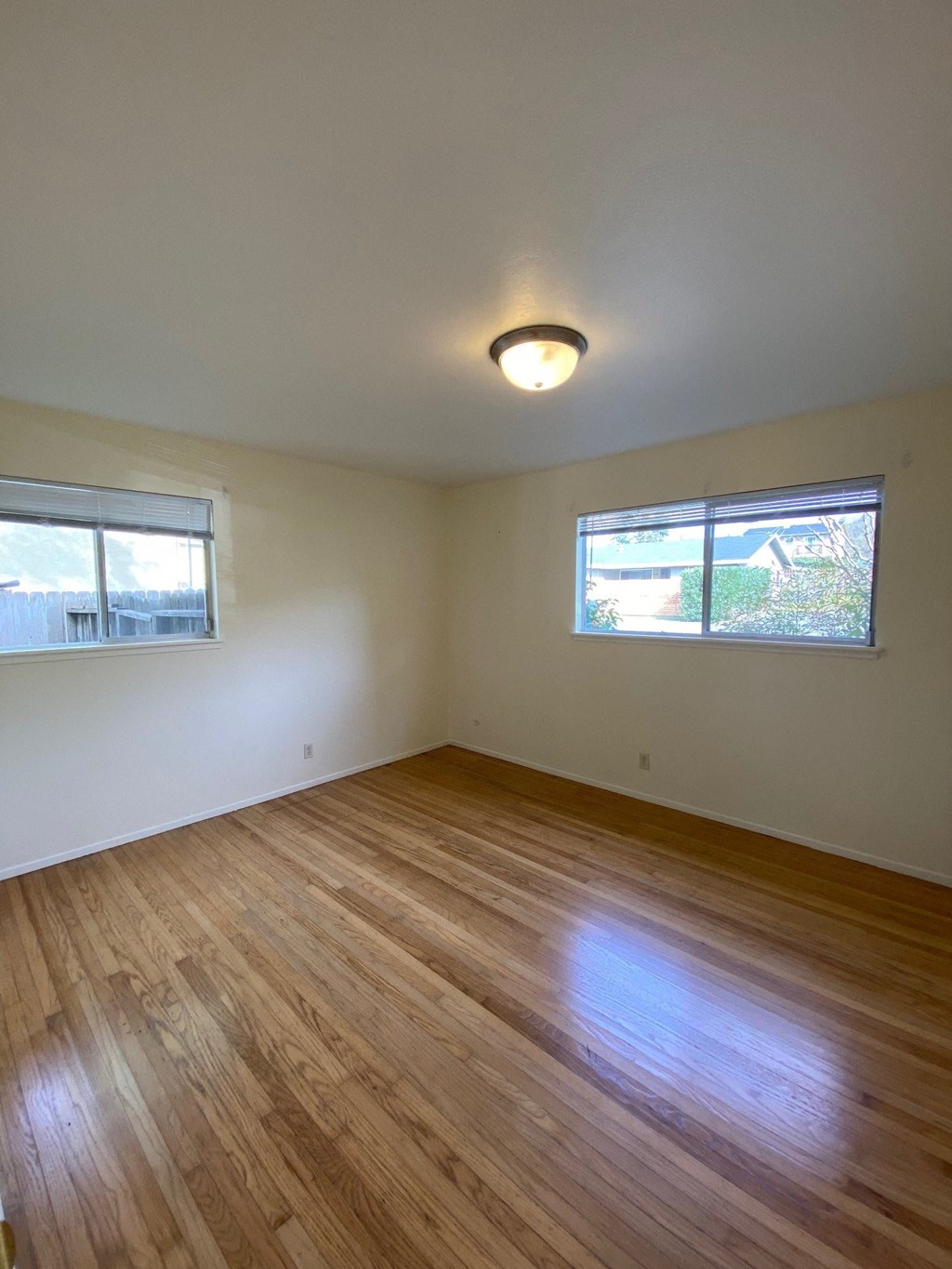 the living room of an empty house with wooden floors and two windows