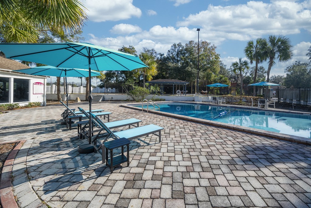 A pool area with a blue umbrella and a brick patio. at Red Bay Apartment Complex, Jacksonville, FL, 32211