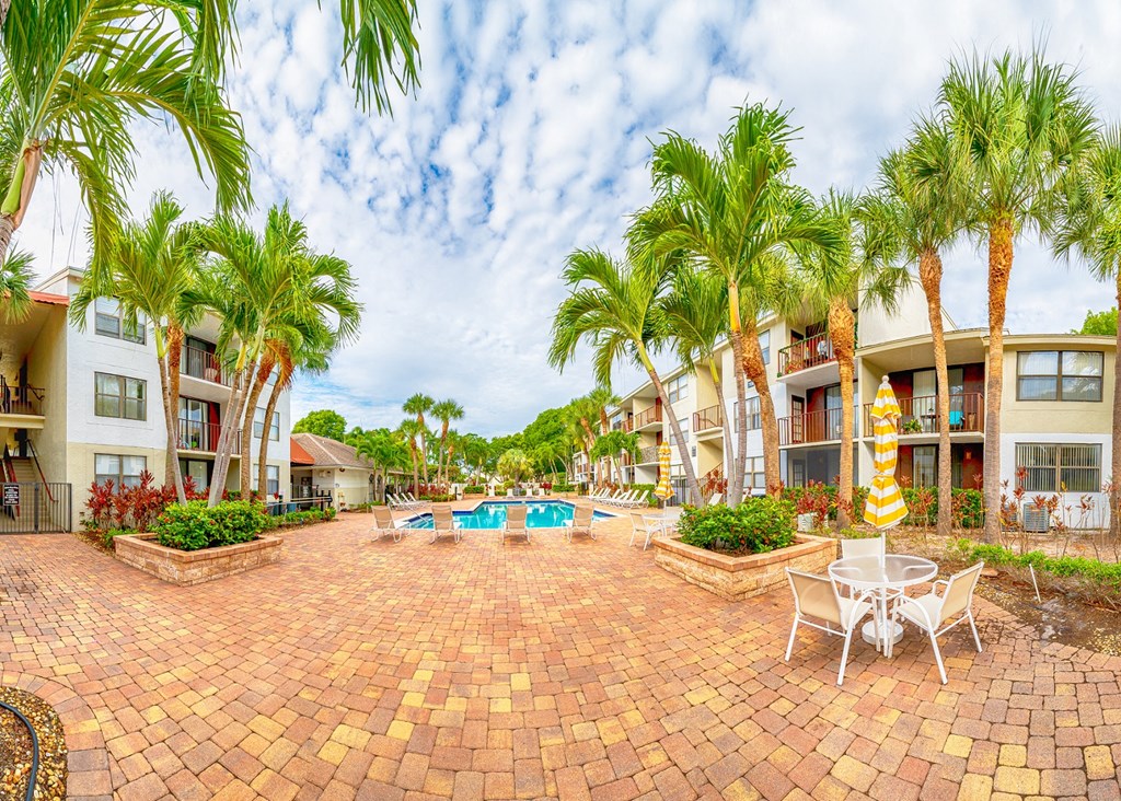 a patio with a swimming pool and palm trees in front of apartment buildings