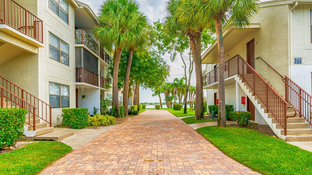 a pathway between two apartment buildings with palm trees