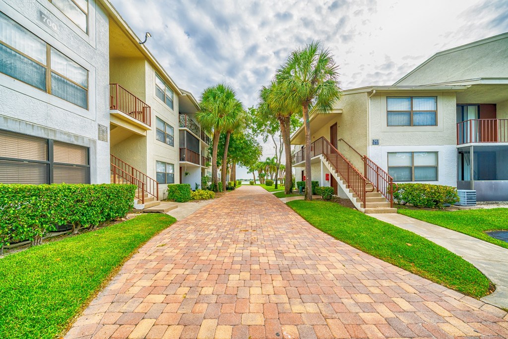 a brick pathway between two apartment buildings with palm trees