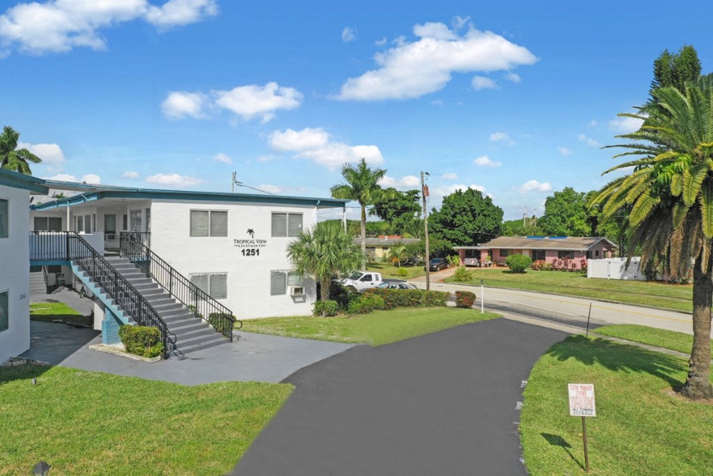 a white building with a blue roof and a palm tree in front of it
