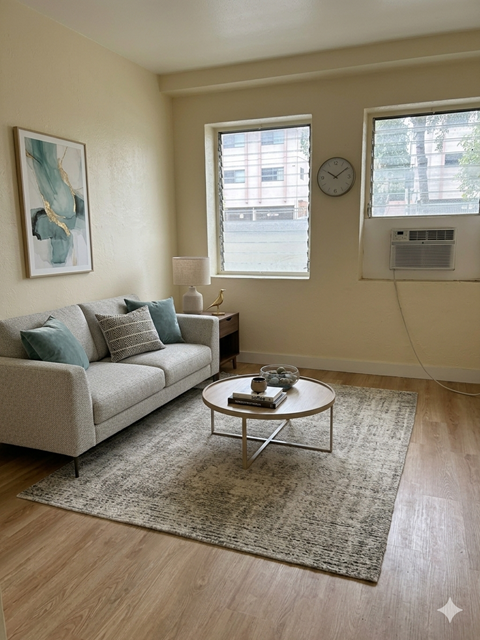 A living room with a couch, a coffee table, a rug, a clock, and a painting on the wall.