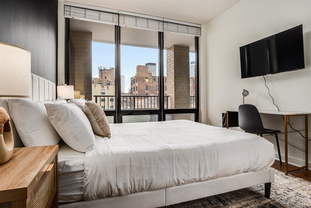 A bedroom with a large bed, a chair, and a flat-screen TV mounted on the wall.