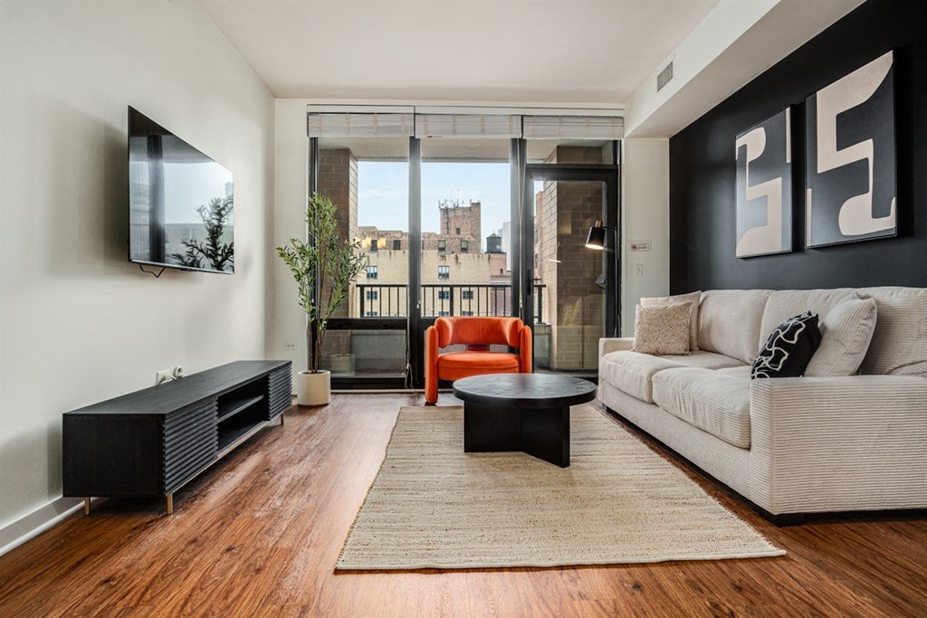 A living room with a white couch, a black coffee table, and a flat screen TV mounted on the wall.