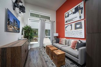 a living room with an orange accent wall and gray couches