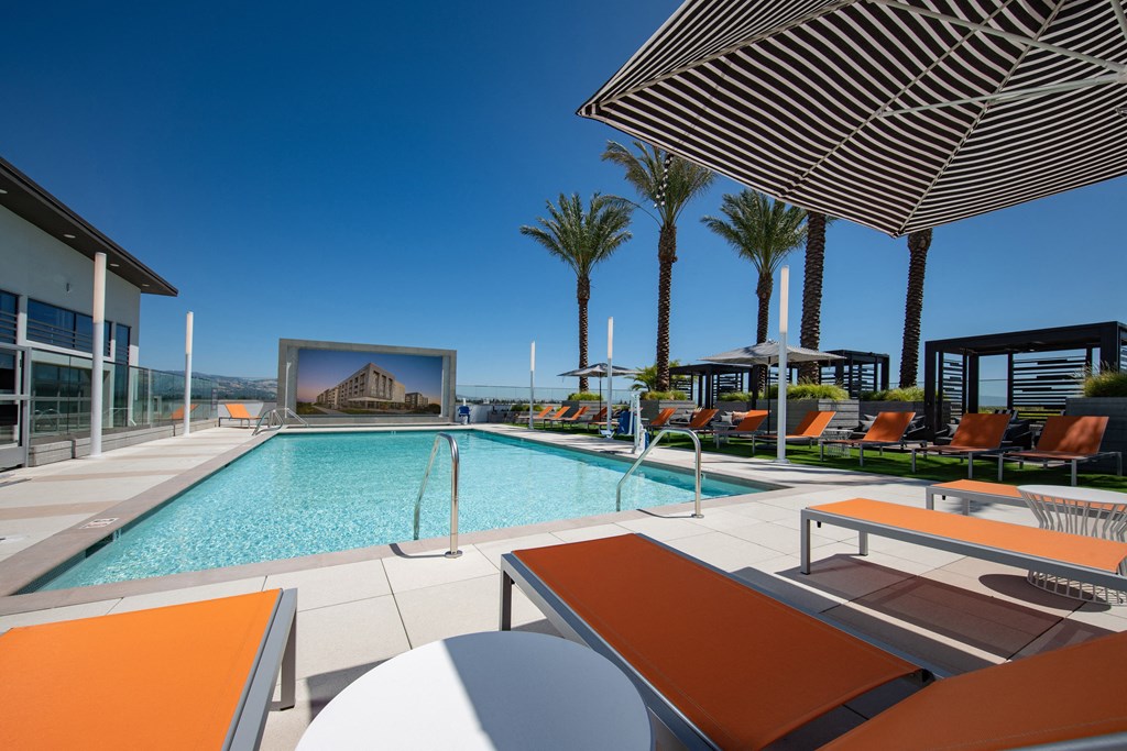 a large swimming pool with lounge chairs and umbrellas on a sunny day