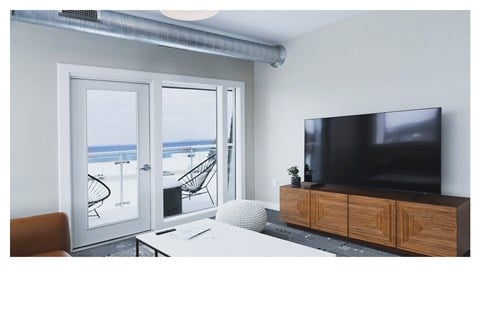 A modern living room with a television, chair, and a view of the beach through the sliding glass doors.