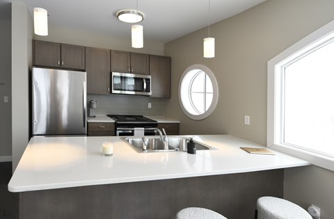 A modern kitchen with a stainless steel refrigerator, microwave, and a round window above the sink.