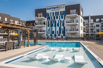A pool with white chairs and a building with a sign that says "current 812" in the background.