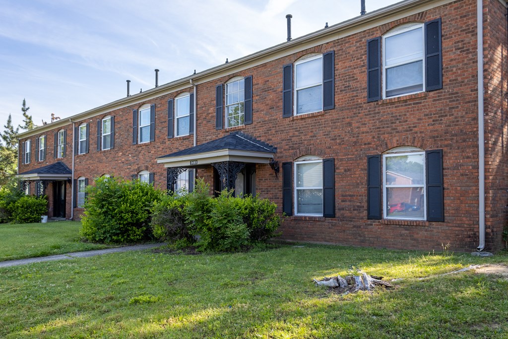 a brick apartment building with a green lawn in front of it