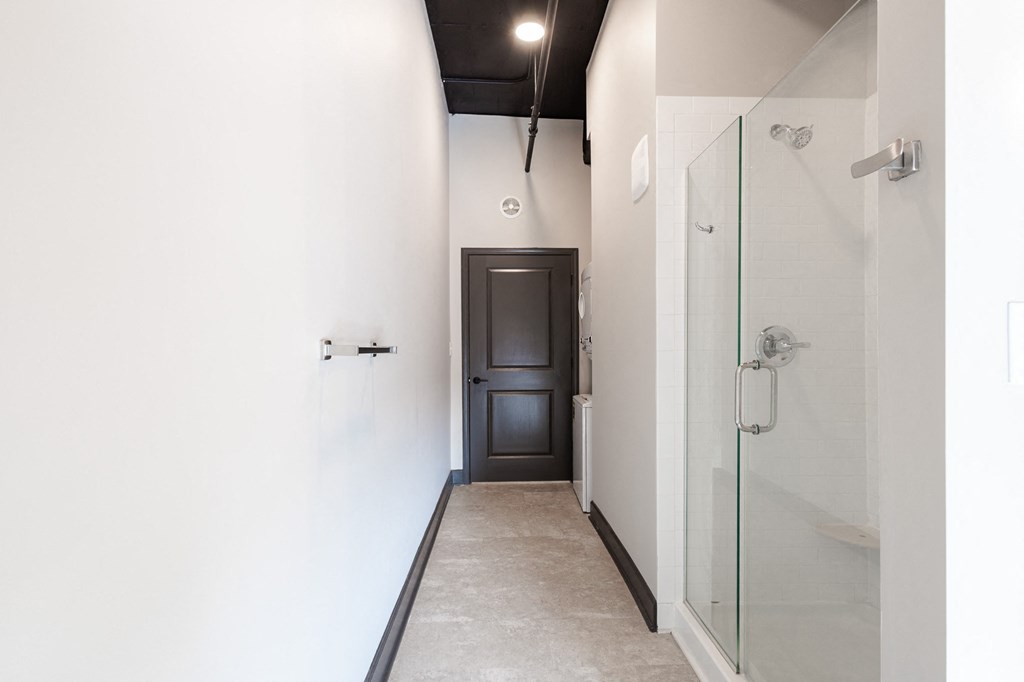 a hallway with white walls and a white tile floor with a glass shower door