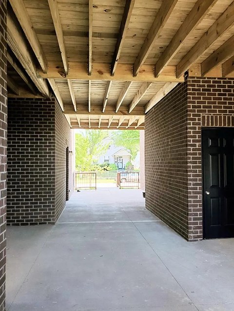 A long outdoor hallway with a black door at the end.