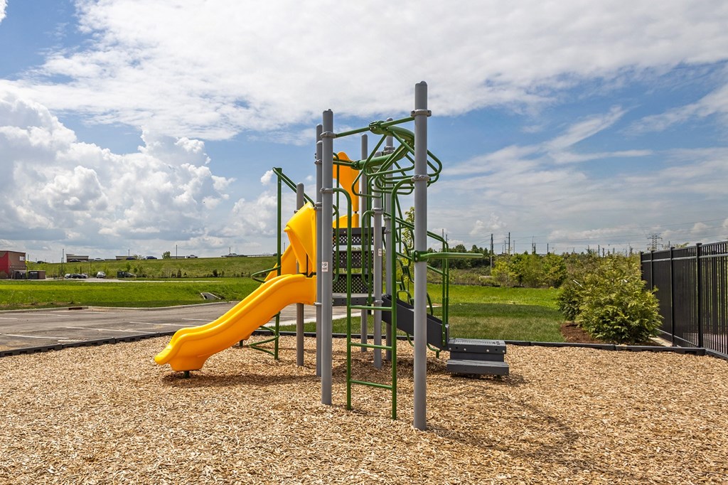 A playground with a yellow slide and a green climbing structure at The Warren Apartments, Indiana