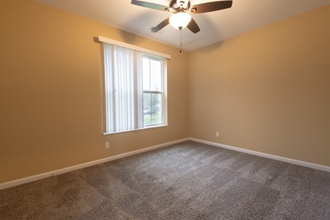 A room with a ceiling fan and a window with curtains.