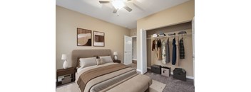 A bedroom with a large bed and a closet with clothes hanging.