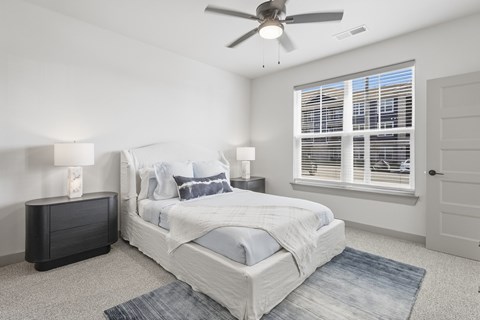 A bedroom with a large bed, a ceiling fan, and a window with blinds at The Warren Apartments, Jeffersonville, IN