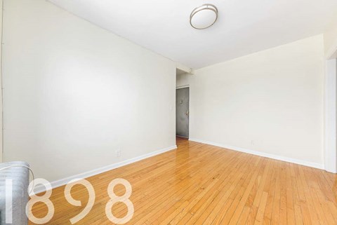 A room with wooden floors and a white wall with a door in the background.