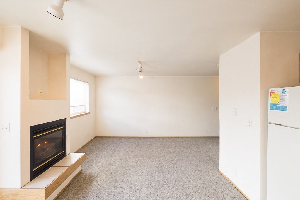an empty living room with a fireplace and a refrigerator