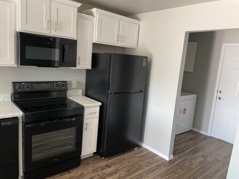 A black refrigerator sits in a kitchen with white cabinets and black appliances.