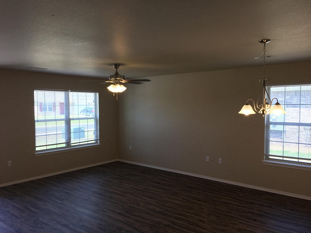 an empty living room with a ceiling fan and two windows