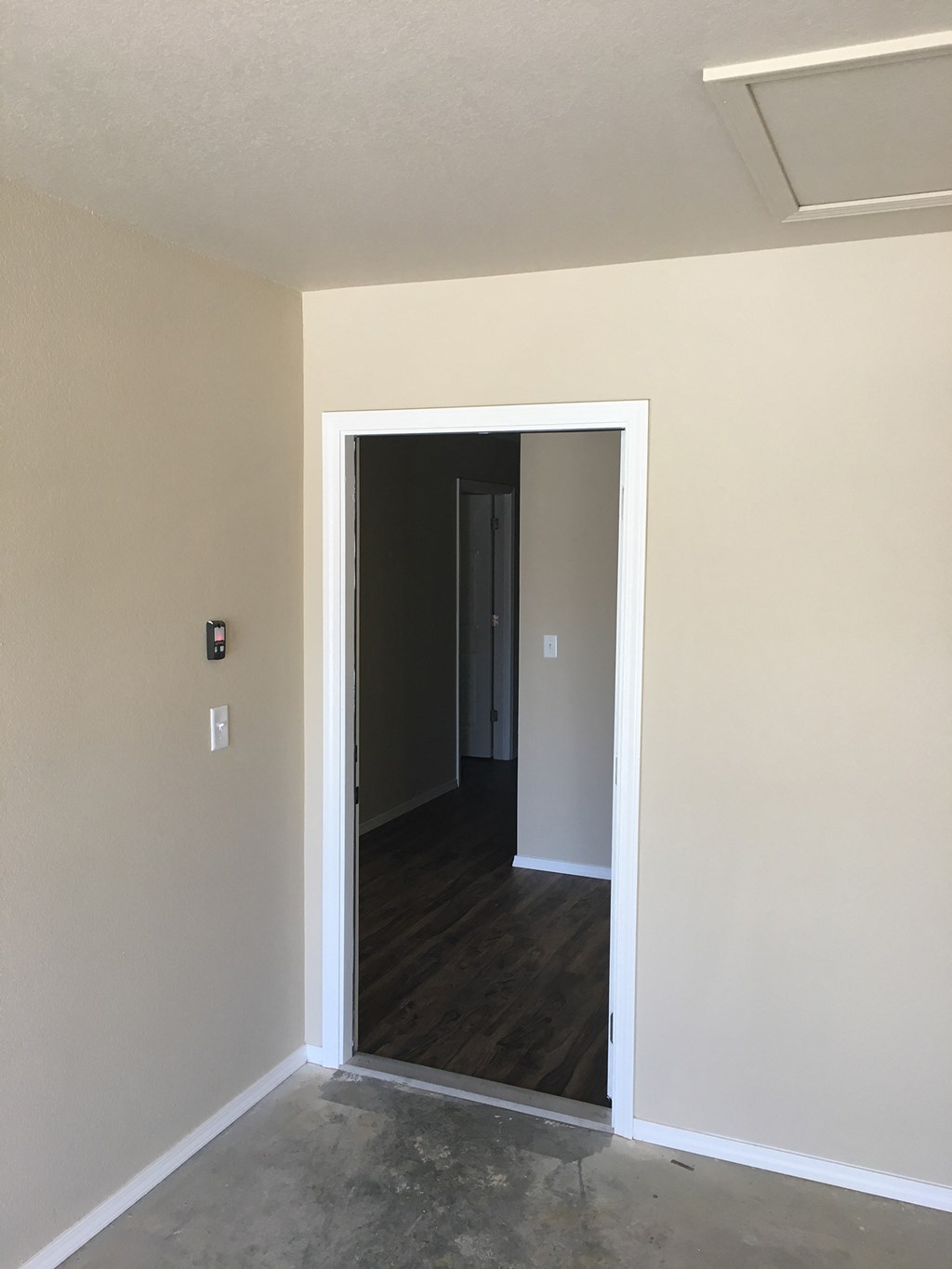 an empty room with a door open to a hallway and a door into a bedroom